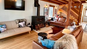 A cozy living room with a fireplace, leather sofas, and a wooden staircase. - Cuff'n'Collar Stable Chalet (Dinner Plain)