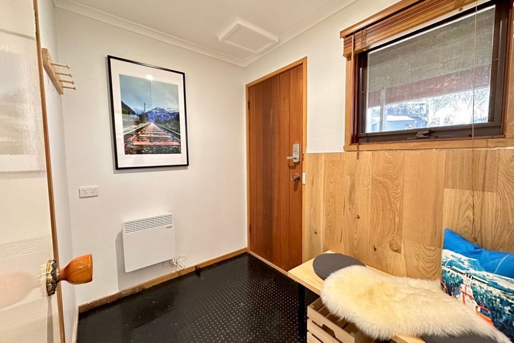 A room with a wooden door, a framed picture on the wall, a window with a view, and a fur throw on a bed.