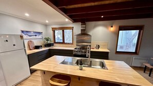 A modern kitchen with a central island, stainless steel appliances, and wooden bar stools. - Cuff'n'Collar Stable Chalet (Dinner Plain)