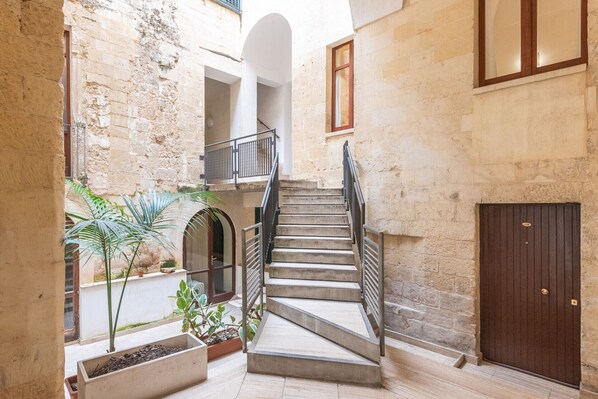 A stone staircase leading to an upper level, surrounded by potted plants and a wooden door.