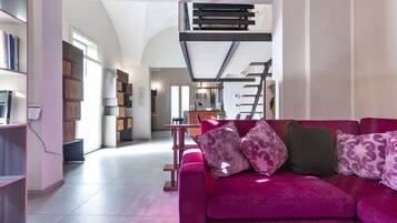 Ein modernes Wohnzimmer mit einem leuchtend rosafarbenen Sofa, einer Treppe und einer dahinterliegenden Küchenzeile.