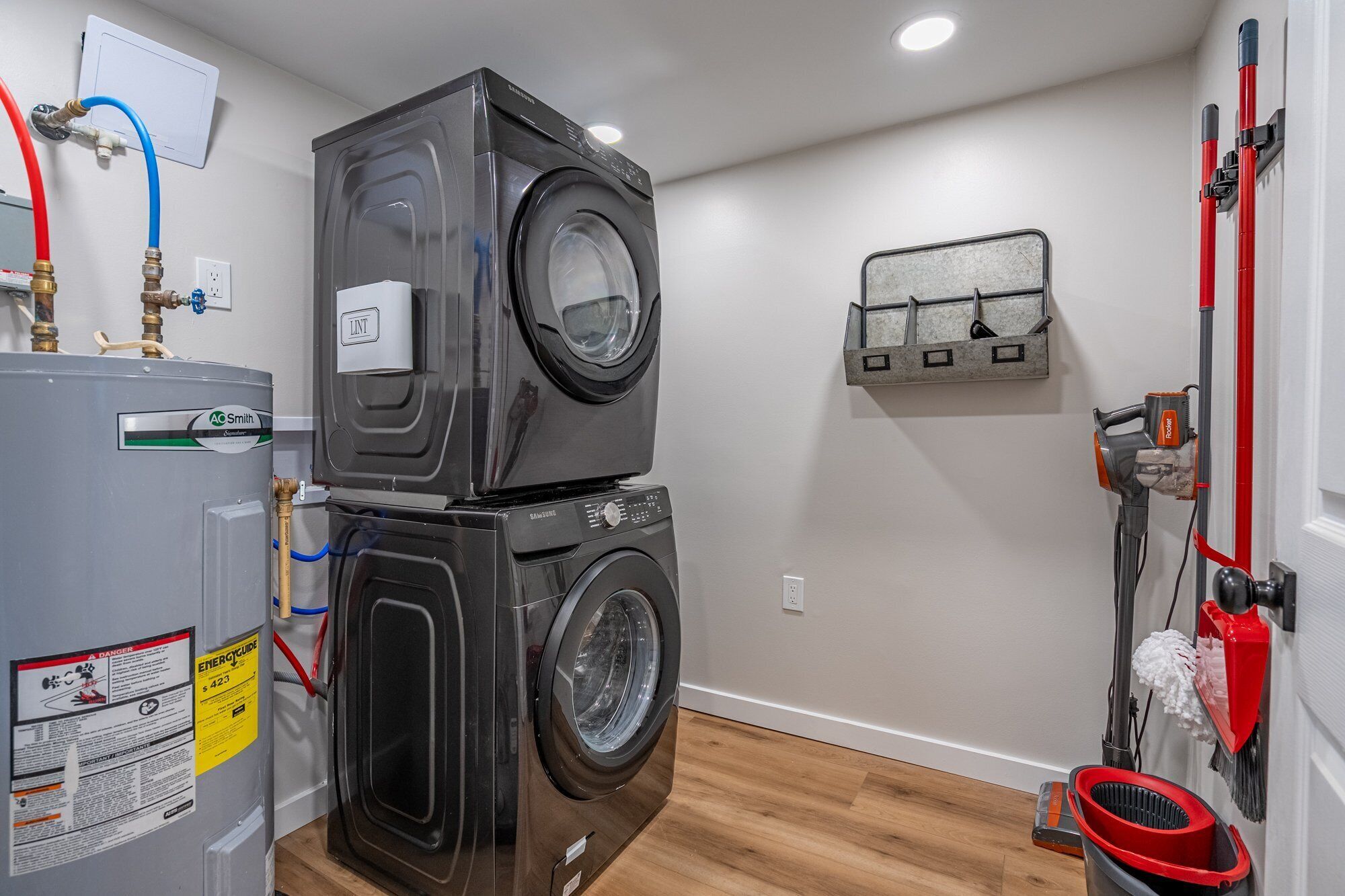 A laundry room with stacked washers and dryers, a water heater, and a wall-mounted toolbox.