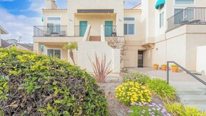 A two-story house with a beige exterior, a balcony on the second floor, and a small garden with yellow and purple flowers. - 357 Ocean View (Pismo Beach)
