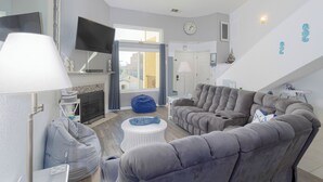 A modern living room with grey sofas, a white coffee table, and a blue bean bag. A flat-screen TV is mounted on the wall, and there is a fireplace in the background. - 357 Ocean View (Pismo Beach)
