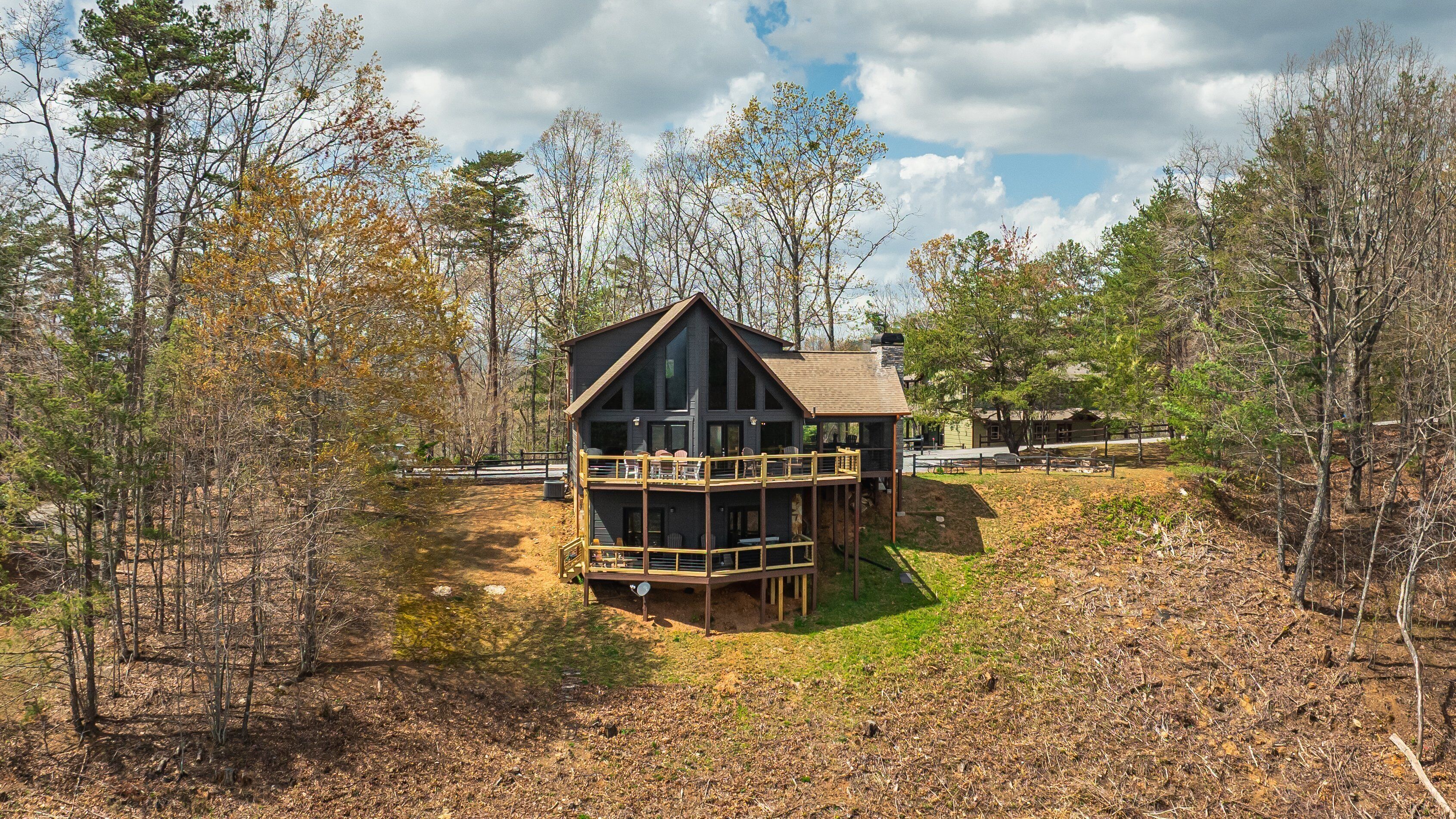 A cabin with a deck and a covered porch, surrounded by trees and a dirt path.
