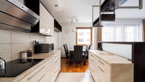 A modern kitchen with a built-in stove, black chairs, and a dining table. - Metro Wilanowska Cosy Apartment (Warszawa)