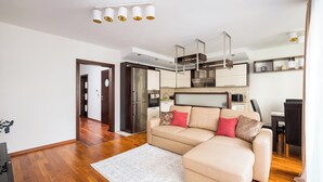 A modern living room with a beige sectional sofa, a white rug, and a kitchen area with stainless steel appliances. - Metro Wilanowska Cosy Apartment (Warszawa)