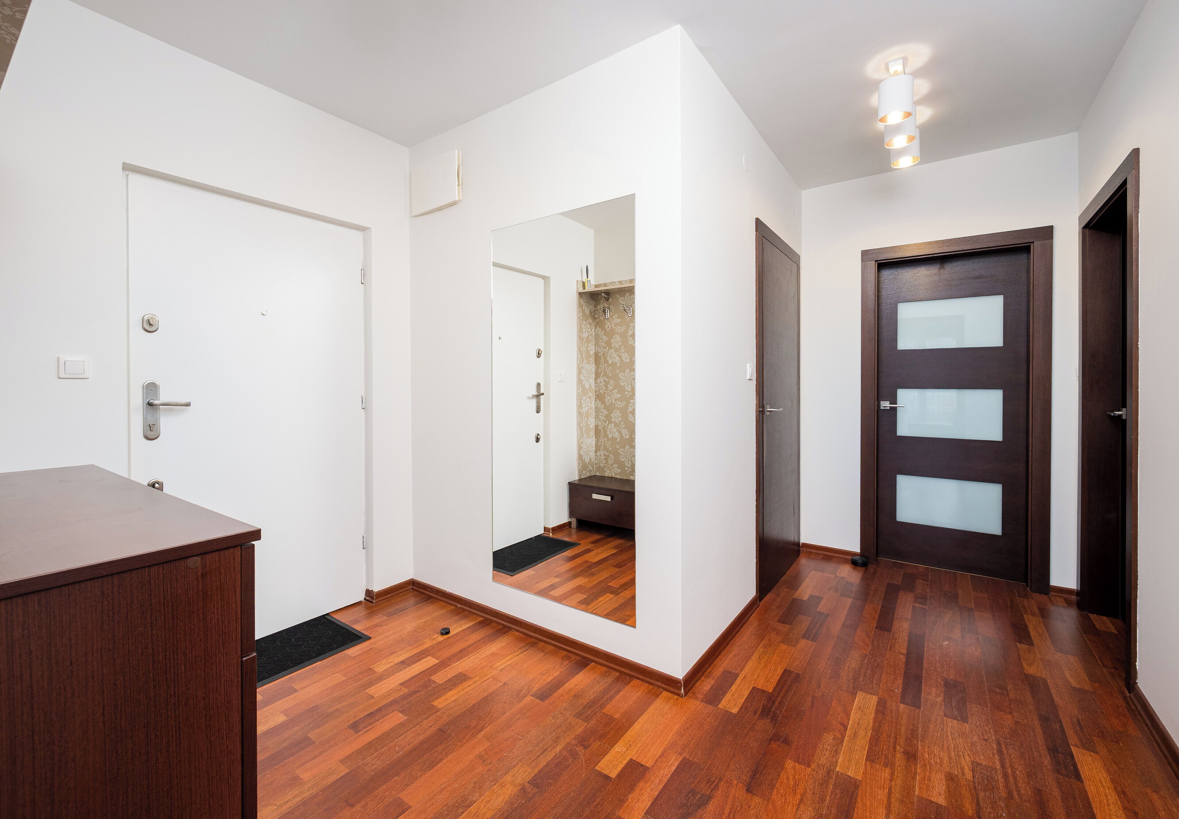 Una stanza con pavimento in legno, pareti bianche, una porta in legno scuro e una porta bianca.