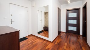 A room with a wooden floor, white walls, a dark wooden door, and a white door. - Metro Wilanowska Cosy Apartment (Warszawa)