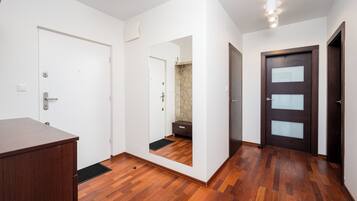 Una stanza con pavimento in legno, pareti bianche, una porta in legno scuro e una porta bianca.
