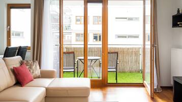 Un soggiorno con divano, tavolino da caffè e una porta scorrevole in vetro che dà su un balcone con vista sul quartiere.