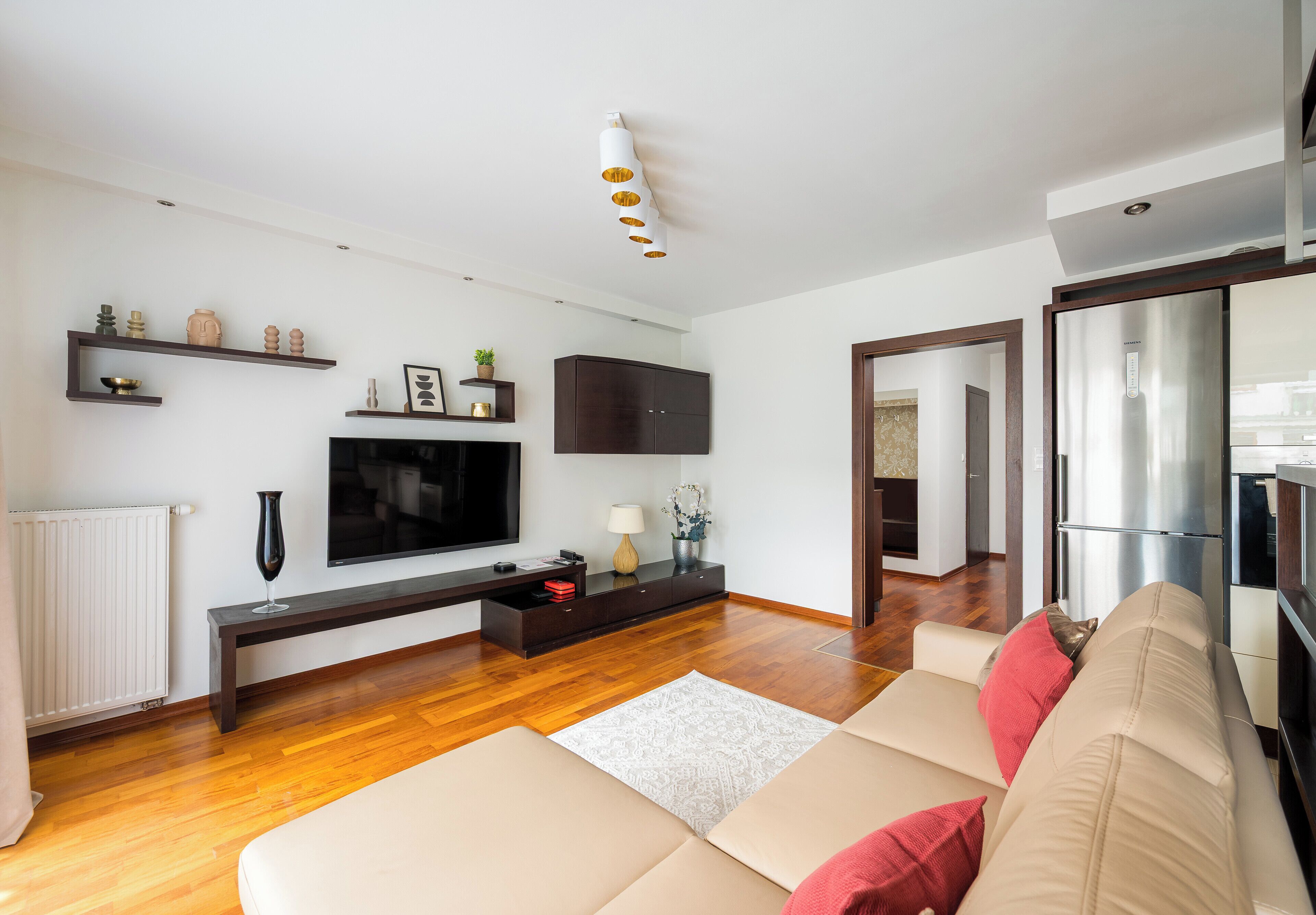 Un soggiorno moderno con un divano, una TV, un pavimento in legno e una zona cucina visibile attraverso una porta aperta.