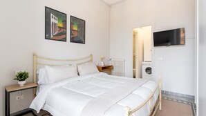 Ein Schlafzimmer mit Bett, Fernseher, Heizkörper und Waschmaschine.