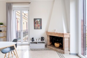 A modern living room with a fireplace, a dining area, and a large window with a view of buildings.