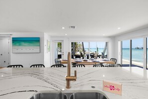 A modern kitchen with a marble countertop, a sink, and a view of a beach and ocean through large windows.