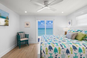 A bedroom with a large bed, a chair, a ceiling fan, and a view of the ocean.