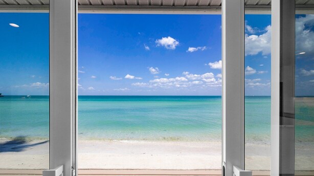 A beach view through a glass door with a clear sky and turquoise water.
