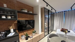 A modern kitchen with a built-in oven, a dining area with a round table, and a living space with a TV mounted on a brick wall. - Studio with pool in downtown RJ (Santa Teresa Rio de Janeiro)
