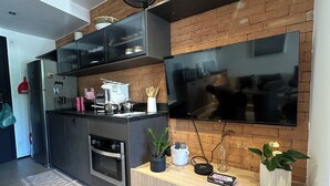 A modern kitchen with a built-in oven, a microwave, and a large flat-screen TV mounted on a brick wall. - Studio with pool in downtown RJ (Santa Teresa Rio de Janeiro)