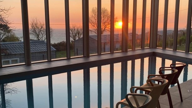 Ein Balkon mit Blick auf den Sonnenuntergang über dem Meer, ausgestattet mit einem Pool und vier Stühlen.
