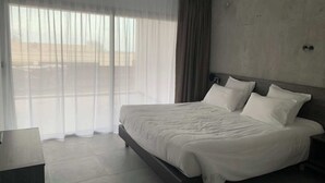 Ein modernes Hotelzimmer mit einem großen Bett, einem Nachttisch und Blick durch transparente Vorhänge.