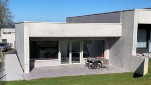 Ein modernes Gebäude mit Flachdach, großen Glasüren und einer Terrasse mit Tisch und Stühlen.