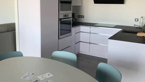 Eine moderne Küche mit Einbauofen, einer Mikrowelle und einem schwarzen Fernseher an der Wand. Im Vordergrund steht ein Esstisch mit Stühlen.