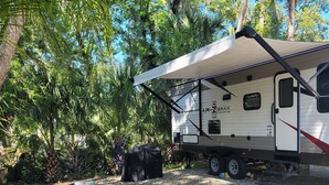 A mobile home with a covered porch, surrounded by lush greenery and palm trees. - Cozy River Retreat 2-bedroom RV with AC, in Homosassa Springs , FL
Lot D15 (Homosassa)