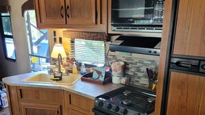 A kitchen with wooden cabinets, a microwave, a stove, and a sink. - Cozy River Retreat 2-bedroom RV with AC, in Homosassa Springs , FL
Lot D15 (Homosassa)