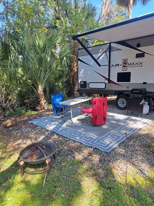 A campsite with a trailer, a table, chairs, and a fire pit. - Cozy River Retreat 2-bedroom RV with AC, in Homosassa Springs , FL
Lot D15 (Homosassa)