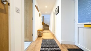 A hallway with wooden flooring, a black and white patterned rug, a wooden bench, and a staircase leading to a room with white walls and a window with blinds.
