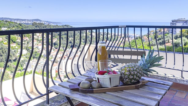 A balcony with a table set for a meal, featuring a pineapple, strawberries, a bottle of juice, and a glass.