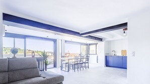 A spacious living area with a grey sofa, a dining table with chairs, and a kitchen area with blue cabinets.