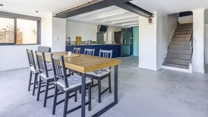 A modern kitchen with dark cabinets, a wooden dining table, and a staircase leading to another level.