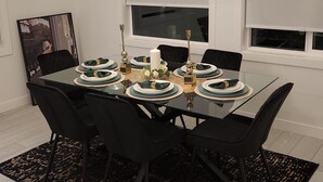 Un comedor moderno con una mesa de vidrio dispuesta para seis personas, sillas negras, un tapete con estampado negro y dorado, y un colgante.