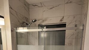 Cabina de ducha con paredes de vidrio, cabezal de ducha de mano, inodoro y una toalla colgada en la pared.