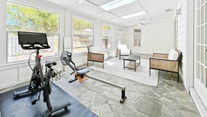 Ein geräumiger Raum mit Deckenventilator, großen Fenstern, Laufband und Steinboden.