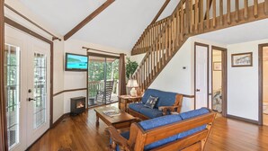 Un vaste salon doté d’un escalier en bois, d’une cheminée et d’une grande fenêtre donnant sur une terrasse.