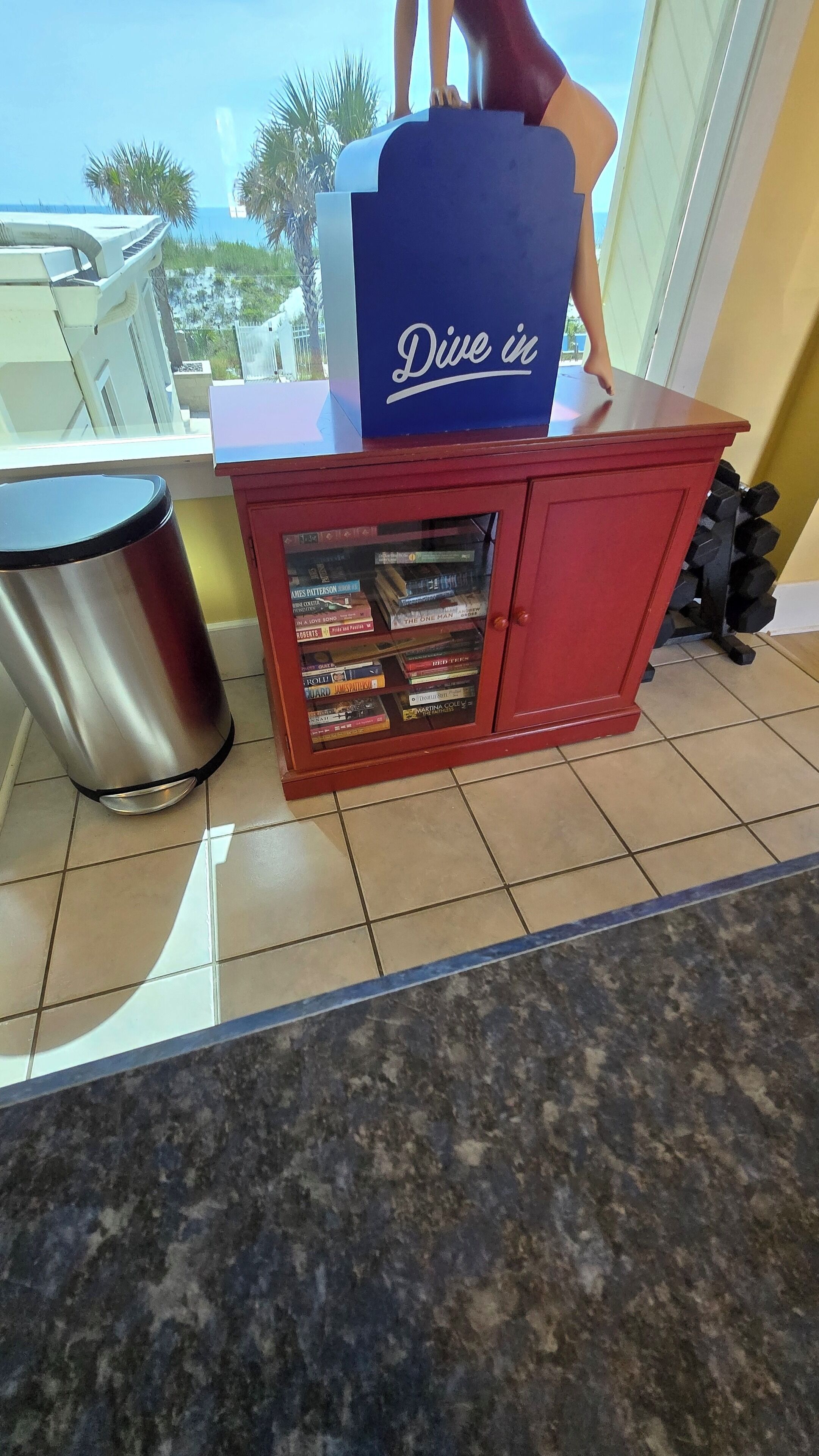 A small red counter with a 'Dive in' sign, a trash bin, and a glass display case with books.