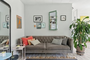 A modern living room with a grey sofa, a large mirror, and a potted plant.