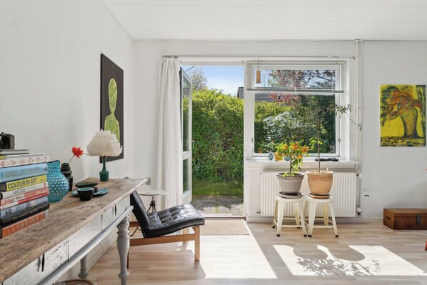 Ein Zimmer mit einem Holztisch, Büchern, einem schwarzen Stuhl, einem Fenster mit Blick auf Grünflächen und einer Heizung.
