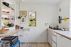 A compact kitchen with white cabinets, a window, and a small dining area with a chair. - A peaceful oasis near the beach and forest (Hundested)