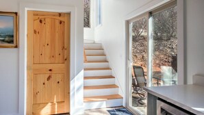 En trappe fører op til en balkon med udsigt over træer og en stol.
