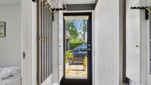 Un pasillo estrecho que conduce a una puerta con vista a un coche aparcado y vegetación al exterior.