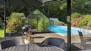 Un espacio al aire libre techado con piscina, invernadero y mobiliario exterior.