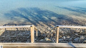 Eine Holzterrasse führt zu einer felsigen Küstenlinie mit klarem Wasser und weit entfernten Hügeln.