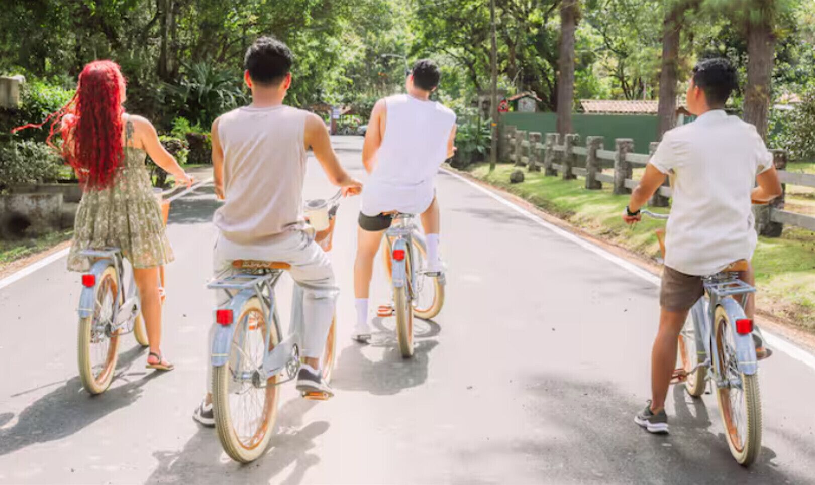 A group of people riding bicycles on a paved road surrounded by greenery.