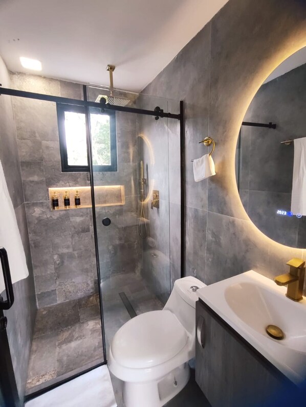 A modern bathroom with a glass-enclosed shower, a white toilet, and a vanity with a gold faucet.