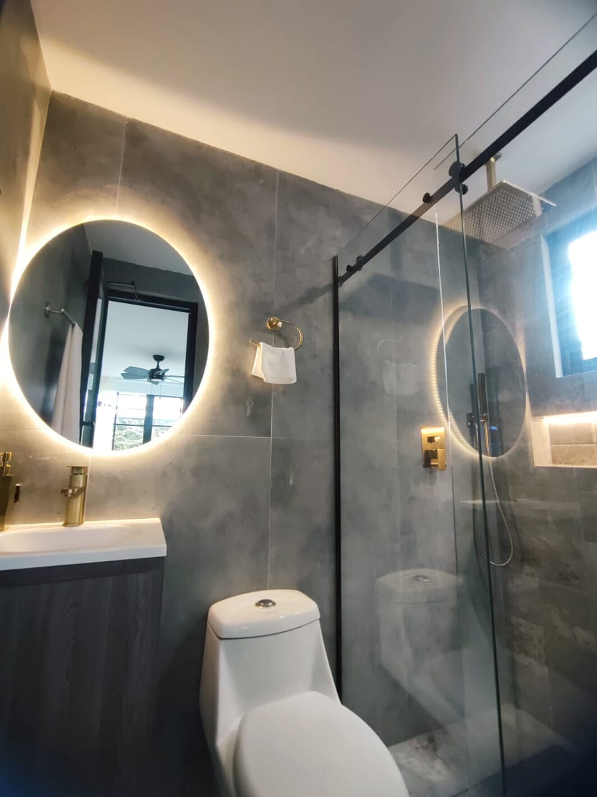 A modern bathroom with a glass shower enclosure, a round mirror, and a toilet.