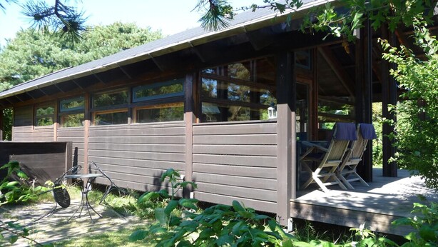 A cabin with a covered porch, a small deck, and a chair. - Cozy cottage close to the beach (Liseleje)